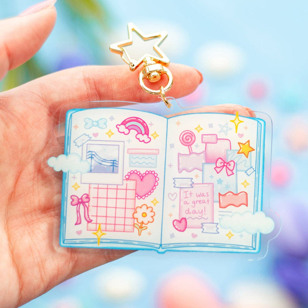 Hand holding a small open book with colorful illustrations and decorative elements against a blurred background.